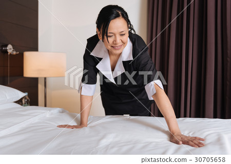 Delighted positive hotel maid cleaning the bed Delighted positive hotel maid cleaning the bed 30705658