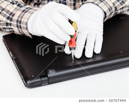 serviceman disassembles laptop with screwdriver 30707494