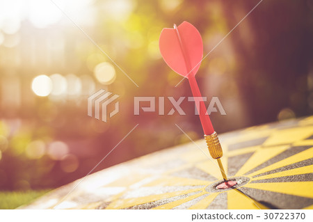 Red dart arrow in the center of dartboard. Blur and bokeh in sunrise time background 30722370
