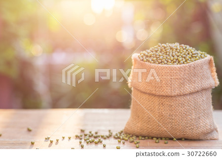 Mung beans in small wooden sack on wooden table. Outdoor shooting with sunlight and green blur bokeh and lens flare effect background Mung beans in small wooden sack on wooden table. Outdoor shooting with sunlight and green blur bokeh and lens flare effect background 30722660