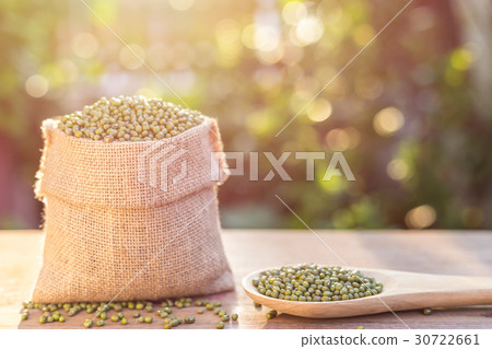 Mung beans in small wooden sack on wooden table. Outdoor shooting with sunlight and green blur bokeh and lens flare effect background Mung beans in small wooden sack on wooden table. Outdoor shooting with sunlight and green blur bokeh and lens flare effect background 30722661
