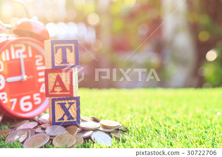 TAX write in color alphabet wood box on stack of Thai baht coin and red alarm clock with right free space for text. For time to pay tax concept. Shot in morning with sunlight and lens flare 30722706