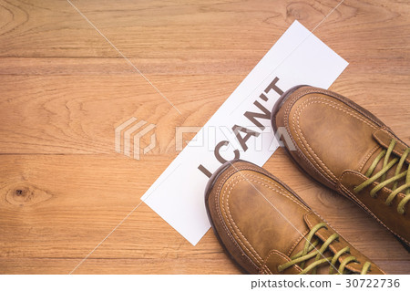 Top view new men shoes step on word "I CAN'T" in white crumpled paper on brown wooden plank Top view new men shoes step on word "I CAN'T" in white crumpled paper on brown wooden plank 30722736