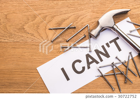 Hammer and nail on top of word "I CAN'T" in white paper on brown wooden plank Hammer and nail on top of word "I CAN'T" in white paper on brown wooden plank 30722752