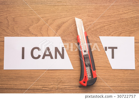 Red cutter blade cutting word "I CAN'T" in white paper on brown wooden plank Red cutter blade cutting word "I CAN'T" in white paper on brown wooden plank 30722757