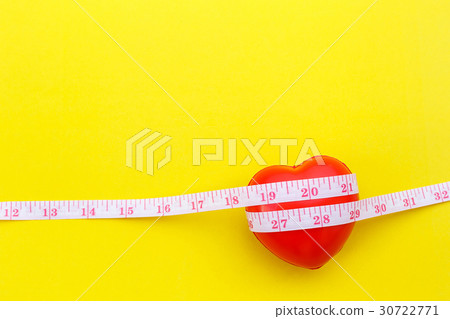 Red heart shape and white measurement tape on yellow background. For heart check up or checking size concept Red heart shape and white measurement tape on yellow background. For heart check up or checking size concept 30722771
