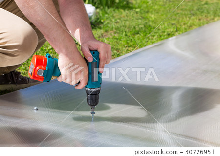 Worker screwing screw into polycarbonate Worker screwing screw into polycarbonate 30726951