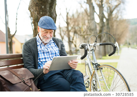 Senior man in town sitting on bench, working on 30728585