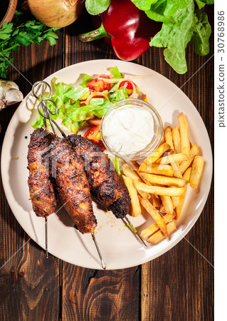 Grilled shish kebab served with fried chips and salad 30768986
