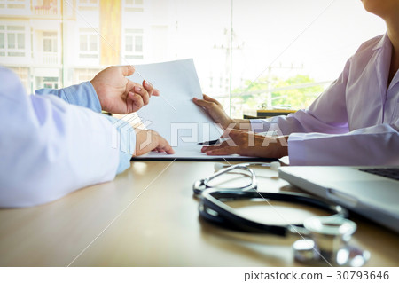 Two doctors discussing patient notes in an office pointing to a Two doctors discussing patient notes in an office pointing to a 30793646