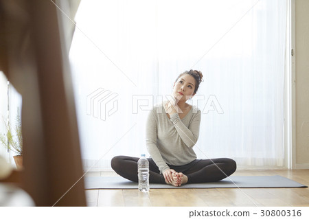 A woman is sitting and cleaning sweat after doing yoga exercise. 30800316