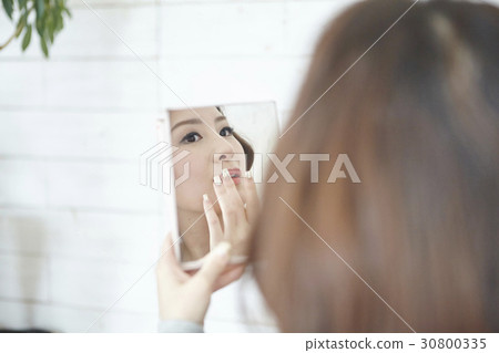 A woman is using mirror to check her make up. 30800335