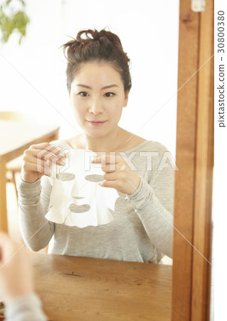 A woman is applying facial mask sheet and looking in the mirror. A woman is applying facial mask sheet and looking in the mirror. 30800380