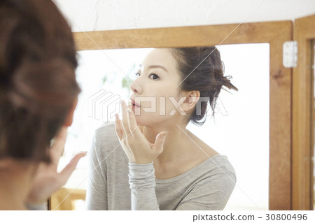 a woman is looking at a mirror and touching her lips. 30800496
