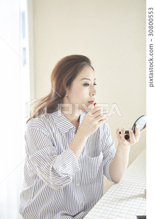 a woman holds a small mirror and makes up by lipstick. 30800553