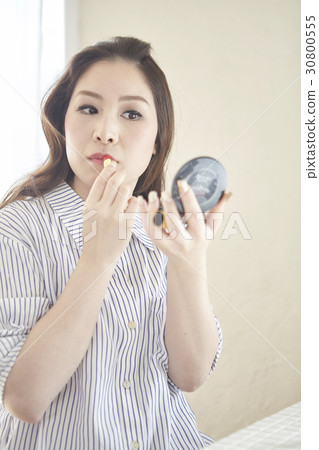 a woman looks at a small mirror and makes up by lipstick. 30800555
