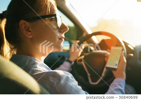 Happy woman uses a navigator in a smartphone while driving a car Happy woman uses a navigator in a smartphone while driving a car 30840699