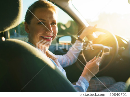 Happy woman uses a navigator in a smartphone while driving a car Happy woman uses a navigator in a smartphone while driving a car 30840701
