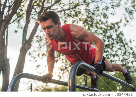 Fit young man doing push ups on horizontal bar 30844488
