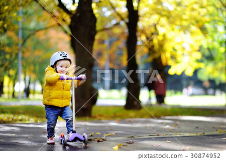Toddler boy in safety helmet learning to ride scooter Toddler boy in safety helmet learning to ride scooter 30874952