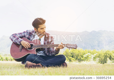 Handsome man playing guitar on green grass Handsome man playing guitar on green grass 30895254
