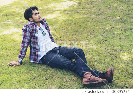Young man sitting on green grass thinking Young man sitting on green grass thinking 30895255