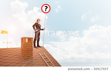 Businessman on brick house roof showing banner with question mark. Mixed media Businessman on brick house roof showing banner with question mark. Mixed media 30917937