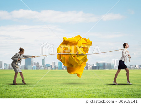 Two women pulling with effort big crumpled ball of paper as creativity sign 30919141