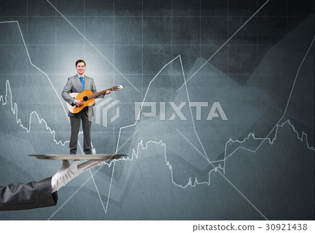 Businessman on metal tray playing acoustic guitar against concrete wall background with charts 30921438