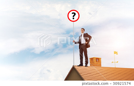 Businessman on brick house roof showing banner with question mark. Mixed media 30921574