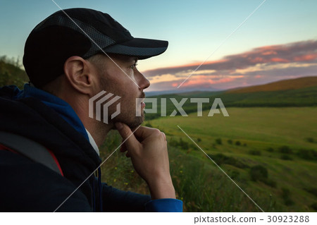 Thoughtful tourist sits on a mountain and looks 30923288