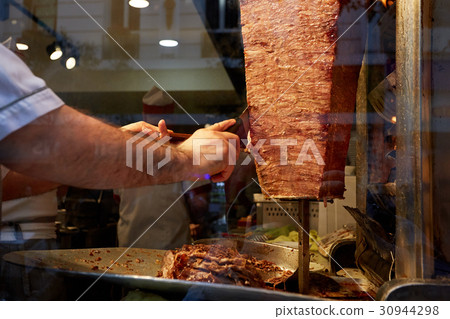 An arm moving to cut the kebab meat 30944298