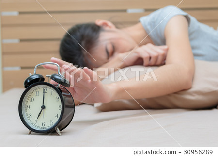 Sleepy woman  extending hand to alarm cock 30956289