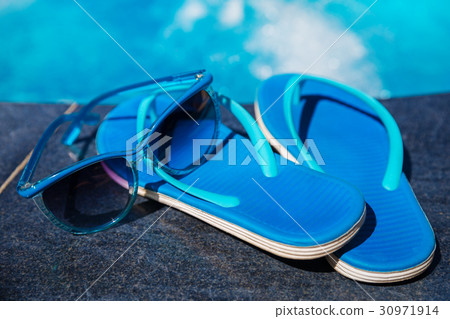 Blue slippers and sun glasses near swimming pool Blue slippers and sun glasses near swimming pool 30971914