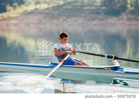 A Young single scull rowing competitor paddles on 30973078