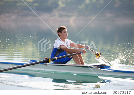 A Young single scull rowing competitor paddles on 30973117