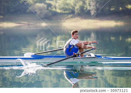 A Young single scull rowing competitor paddles on 30973121