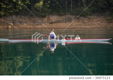 A Young single scull rowing competitor paddles on 30973123