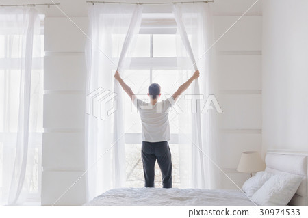 Young man opening window curtains 30974533