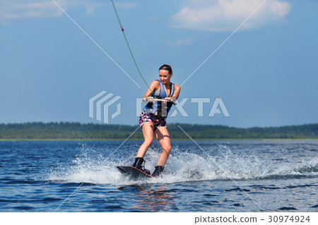 slim woman riding wakeboard on wave of boat 30974924