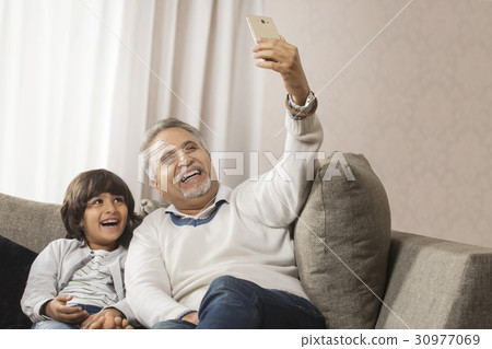 Happy grandfather and grandson taking a selfie together sitting on sofa Happy grandfather and grandson taking a selfie together sitting on sofa 30977069
