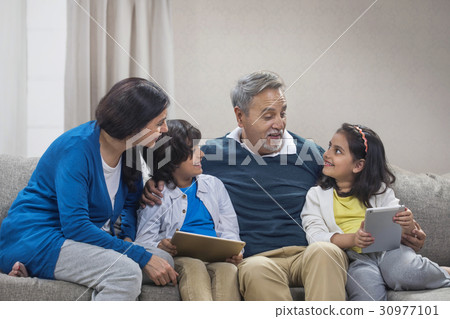 Happy grandchildren using digital tablet with grandparents sitting on sofa 30977101