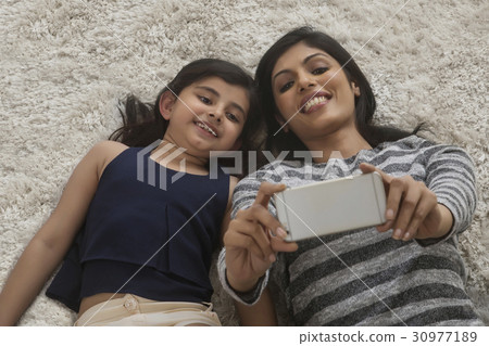 Mother and her little daughter lying on the carpet taking selfie with smartphone 30977189