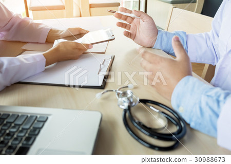 Two doctors discussing patient notes in an office pointing to a 30988673