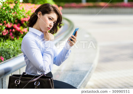 A woman looking at a smartphone thinking A woman looking at a smartphone thinking 30990551