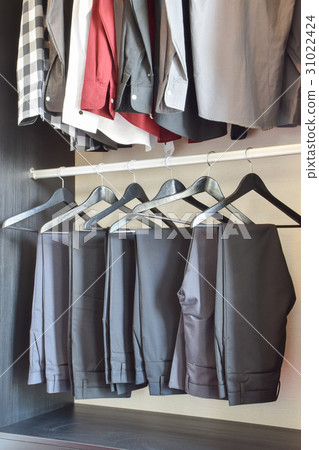 row of pants and shirts hanging in wooden wardrobe row of pants and shirts hanging in wooden wardrobe 31022424