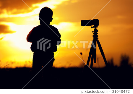 Silhouette picture of boy standing with camera Silhouette picture of boy standing with camera 31040472