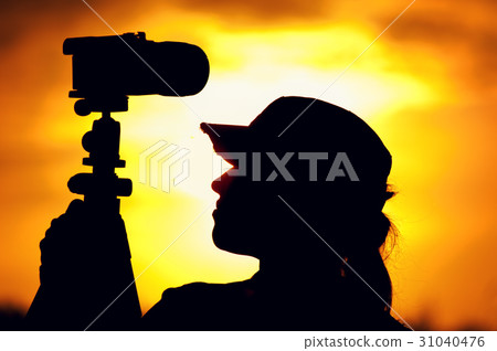 Female photographer standing against setting sun Female photographer standing against setting sun 31040476