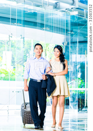 Asian couple walking in hotel lobby with suitcase Asian couple walking in hotel lobby with suitcase 31083552