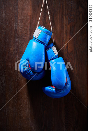 Two blue boxing gloves hanging against wooden 31084552